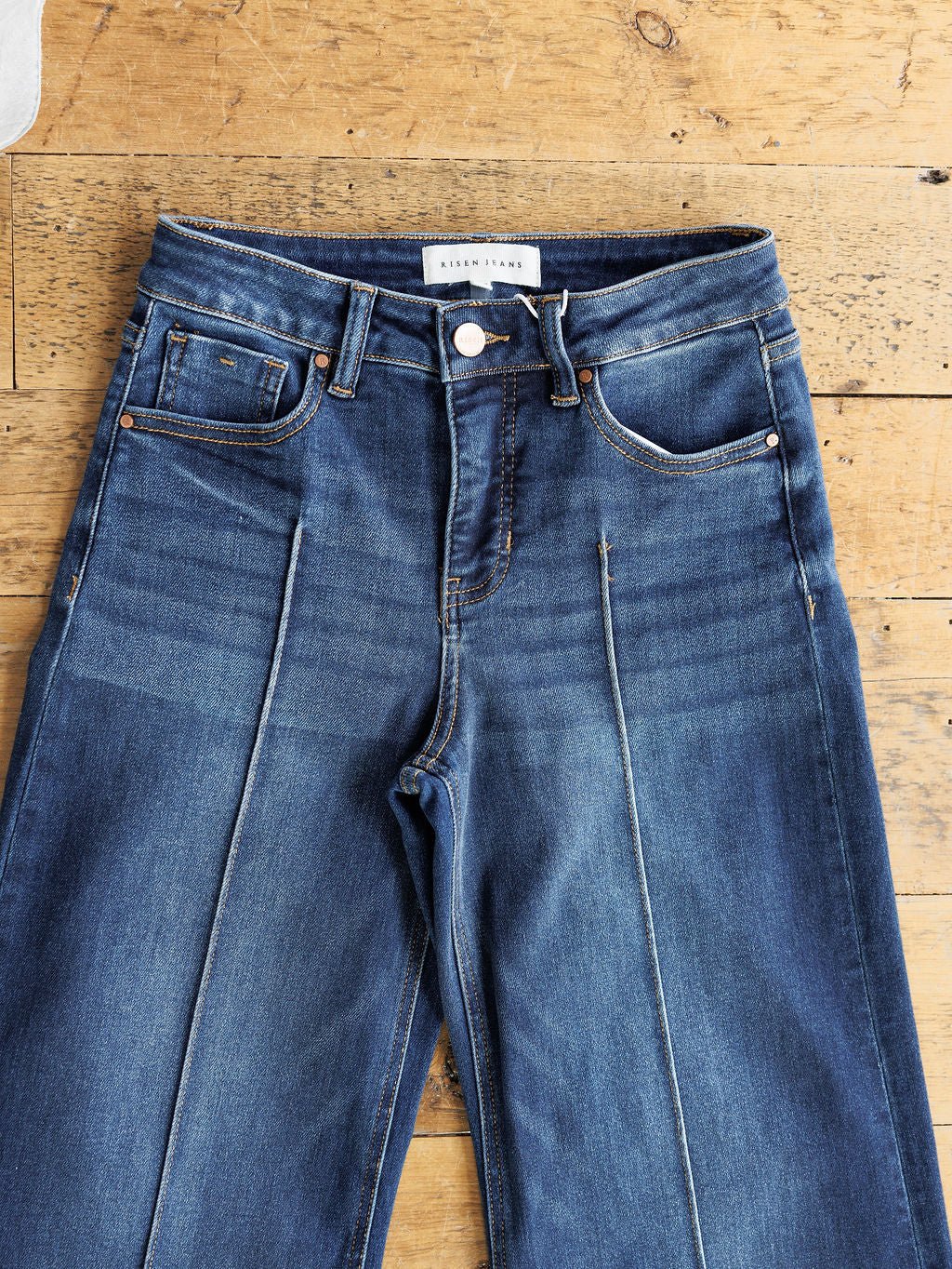 The Dakota High Rise Wide Leg Crop Jean by Savannah Sevens western life{&}style in a dark wash features front and coin pockets, belt loops, button closure, and pressed crease lines. Styled wide leg crop and laid flat on a wooden surface.