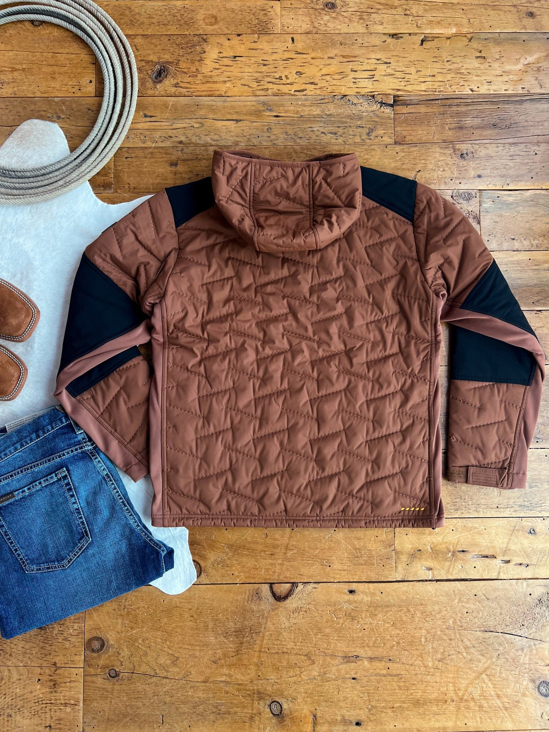 The Davenport Ariat Men's Insulated Jacket by Savannah Sevens western life{&}style is displayed flat on a wooden floor with blue jeans, brown boots, a white hat, and a coiled rope.