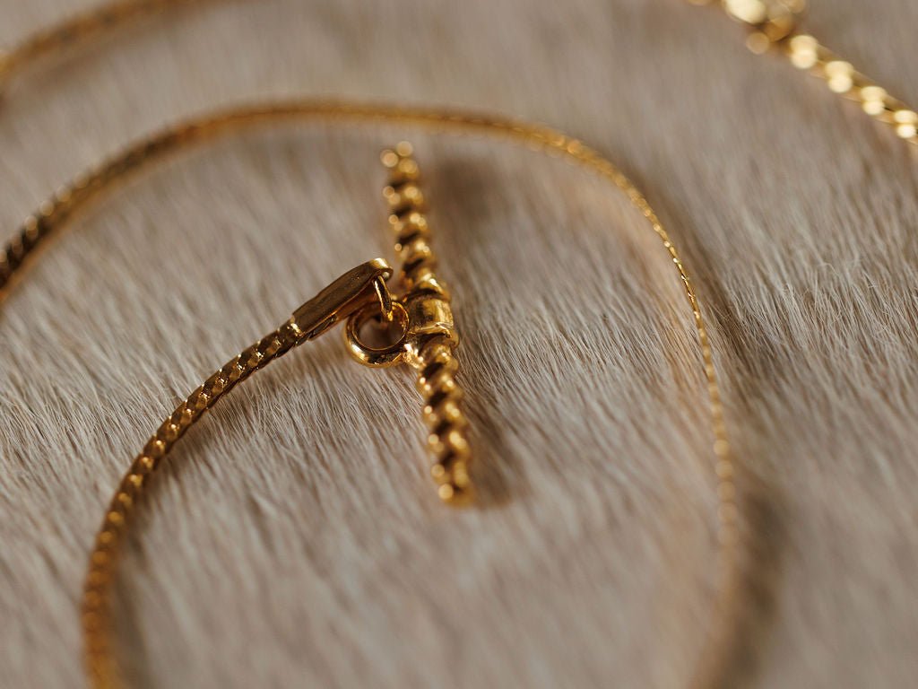 Close-up of the Declo Necklace by Savannah Sevens western life{&}style, featuring a gold filled stainless steel textured chain and bar clasp, displayed on soft, light-colored fabric.
