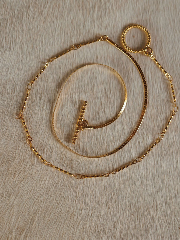 The Declo Necklace by Savannah Sevens western life{&}style, along with two other gold necklaces including a dual strand and a waterproof style, are displayed on a light tan, cowhide surface.