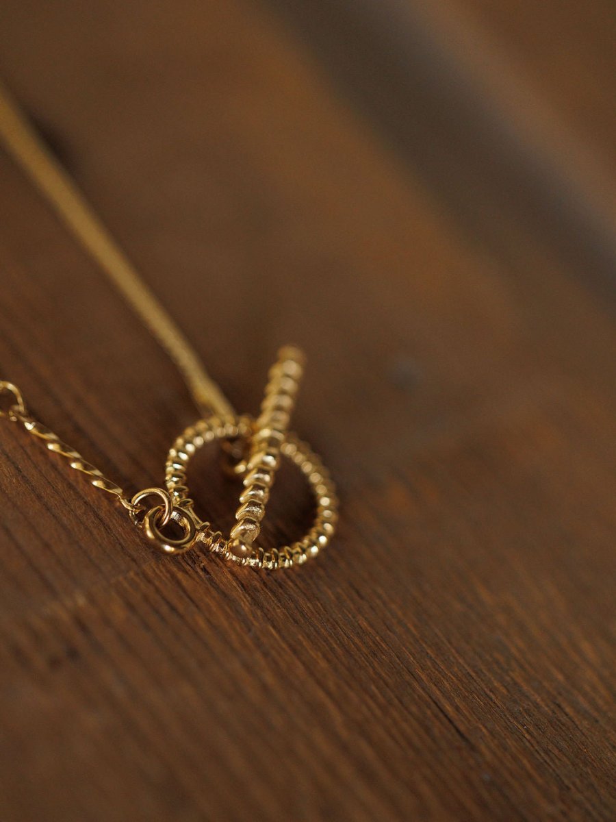 A close-up of the Declo Necklace by Savannah Sevens western life{&}style, featuring a gold filled stainless steel design and beaded toggle clasp, resting on a wooden surface.