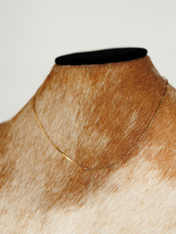 The Declo Necklace by Savannah Sevens western life{&}style, a delicate gold filled stainless steel piece, is displayed on a brown and white animal hide mannequin against a plain white background.