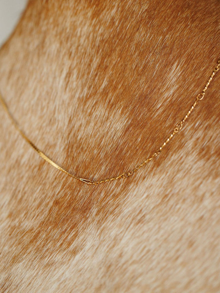 The Declo Necklace by Savannah Sevens western life{&}style lies softly on the short, light brown and white cowhide offering a delicate contrast between its waterproof gold design and the animal’s gentle coat.