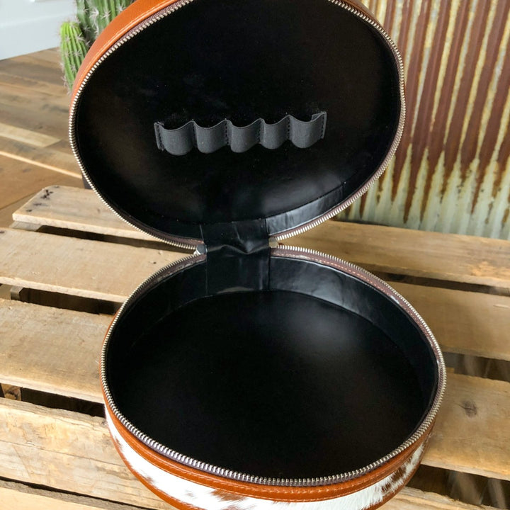 The Del Rey Makeup Case by Savannah Sevens western life{&}style is a round, handmade leather case with a brown and white pattern, black interior, zipper closure, and five lid loops for organizing items.