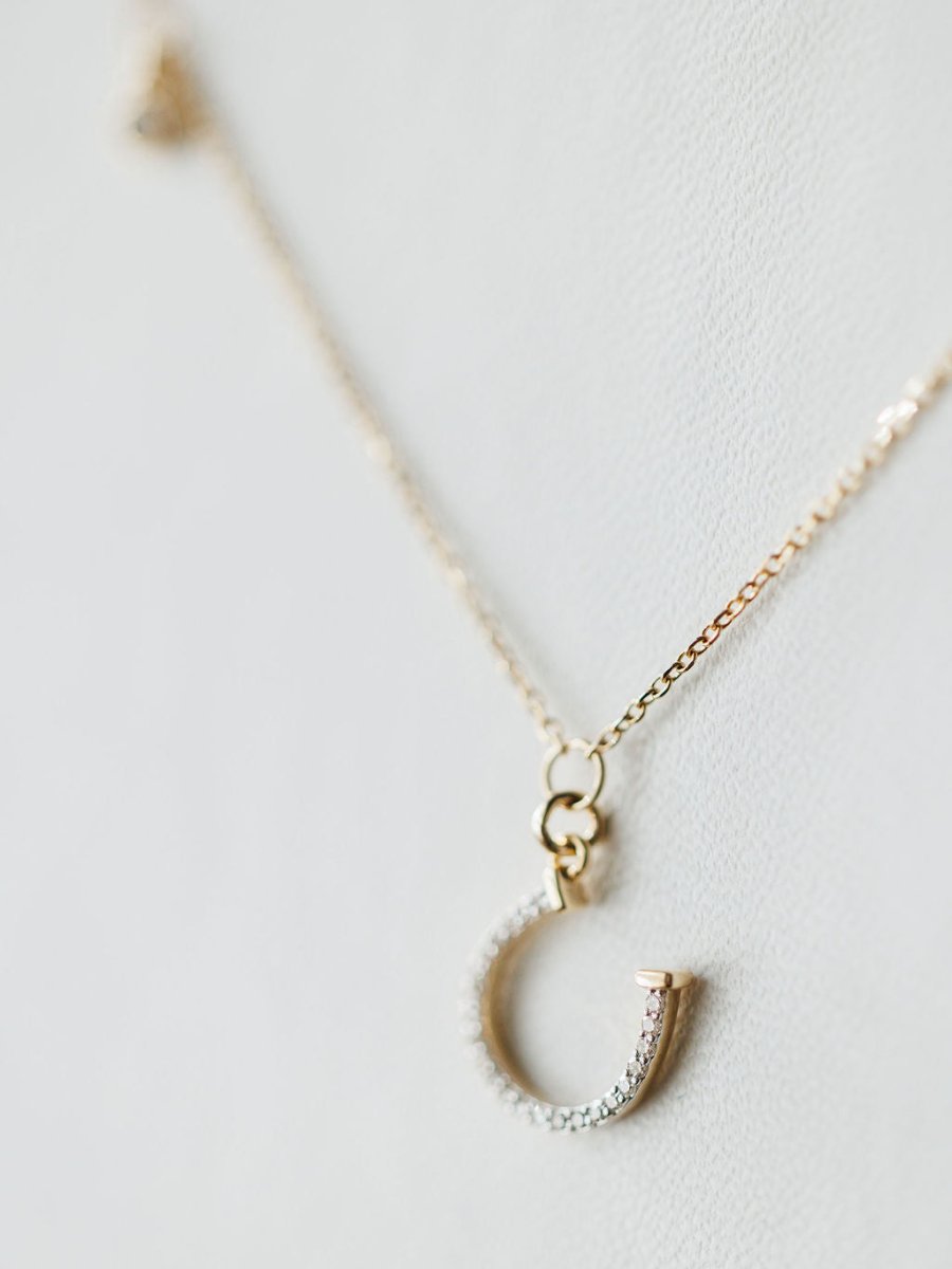 The Diamond Horseshoe Necklace by Savannah Sevens western life{&}style features a 14K gold chain and diamond horseshoe pendant, displayed elegantly against a light, neutral background.