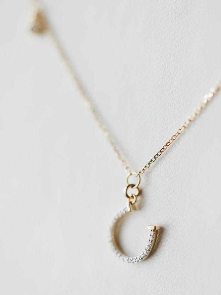 The Diamond Horseshoe Necklace by Savannah Sevens western life{&}style features a 14K gold chain and diamond horseshoe pendant, displayed elegantly against a light, neutral background.
