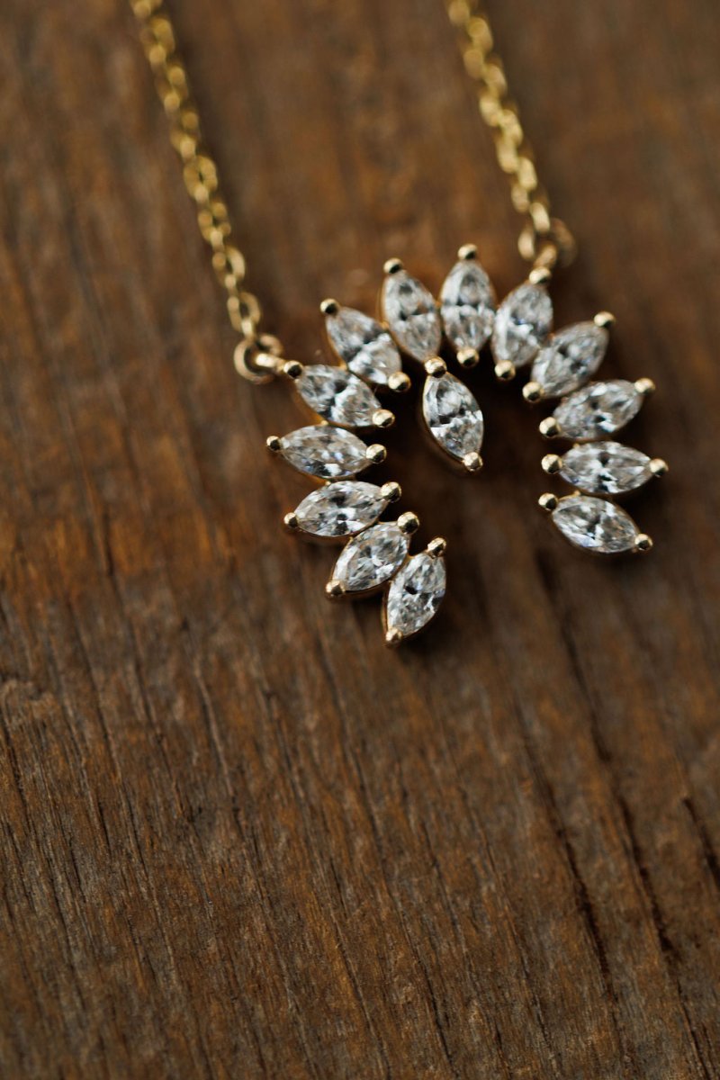 The Savannah Sevens western life{&}style Diamond Naja Necklace showcases marquise-cut lab grown diamonds in a partial circle, set in 14K gold and displayed on a textured wooden surface.