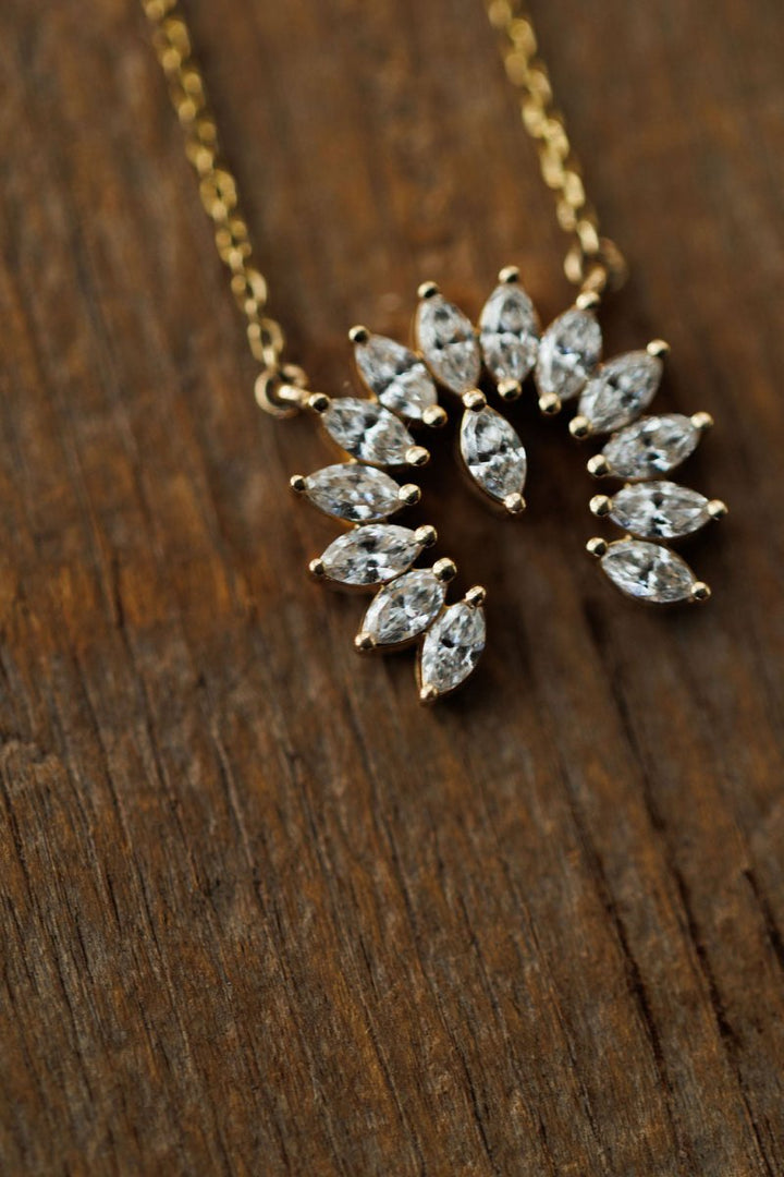 The Savannah Sevens western life{&}style Diamond Naja Necklace showcases marquise-cut lab grown diamonds in a partial circle, set in 14K gold and displayed on a textured wooden surface.