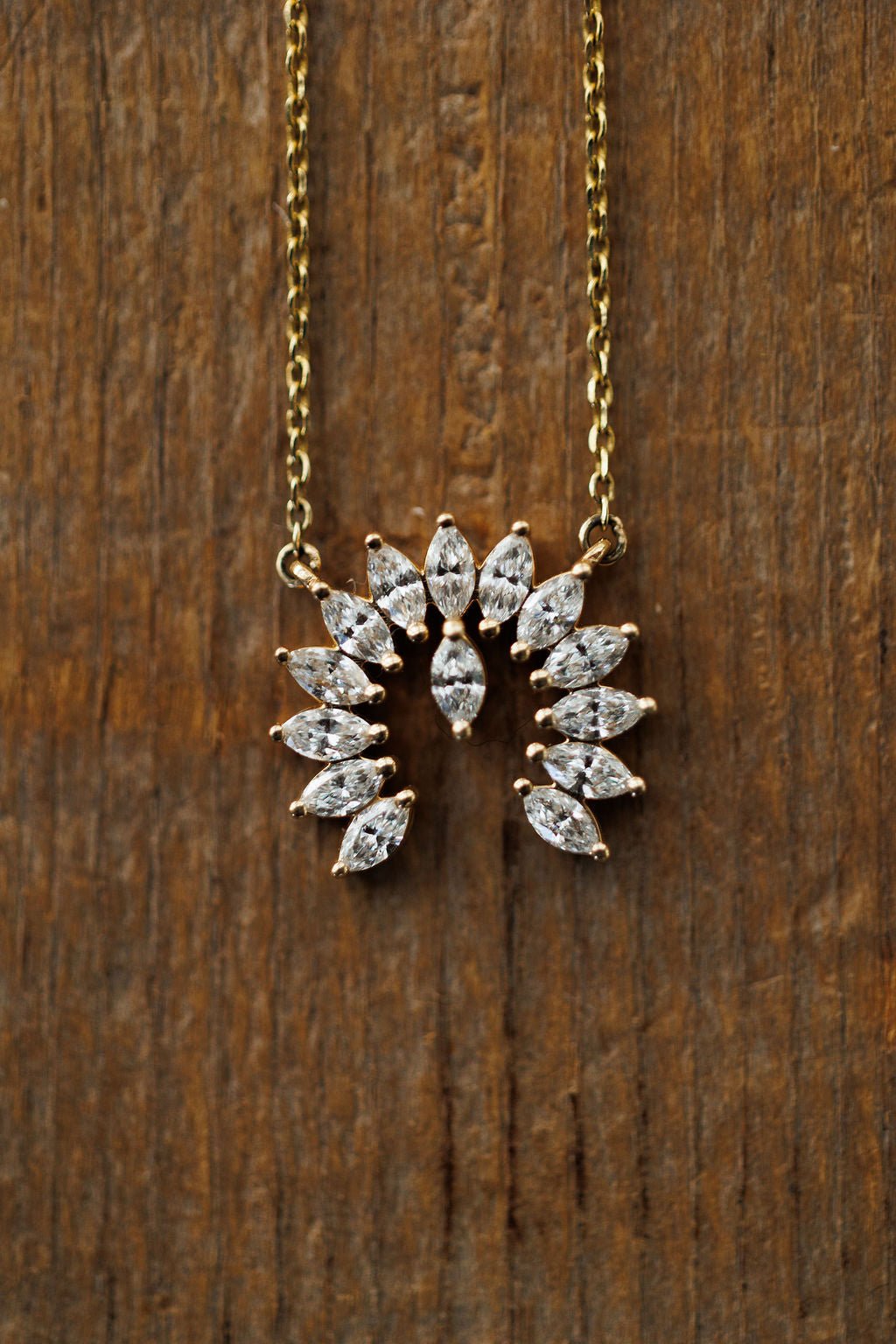 The Diamond Naja Necklace by Savannah Sevens western life{&}style features marquise-cut lab grown diamonds in a fan-pattern partial circle pendant, crafted in 14K gold and shown on a wooden background.