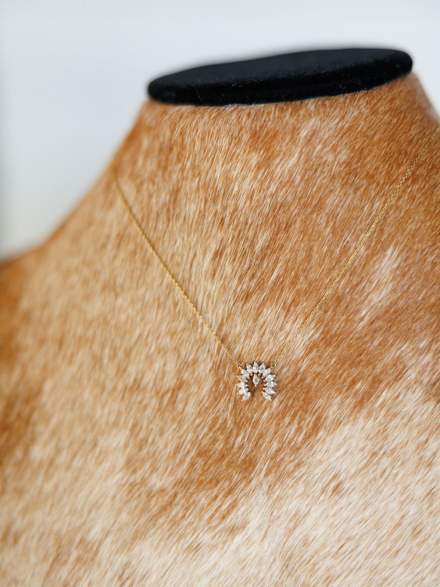 The Diamond Naja Necklace by Savannah Sevens western life{&}style is a 14K gold piece with a crescent-shaped pendant set with lab grown diamonds, shown on a tan and white speckled mannequin bust.