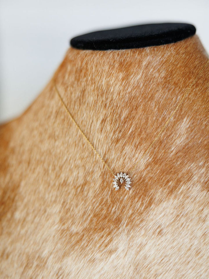 The Diamond Naja Necklace by Savannah Sevens western life{&}style is a 14K gold piece with a crescent-shaped pendant set with lab grown diamonds, shown on a tan and white speckled mannequin bust.