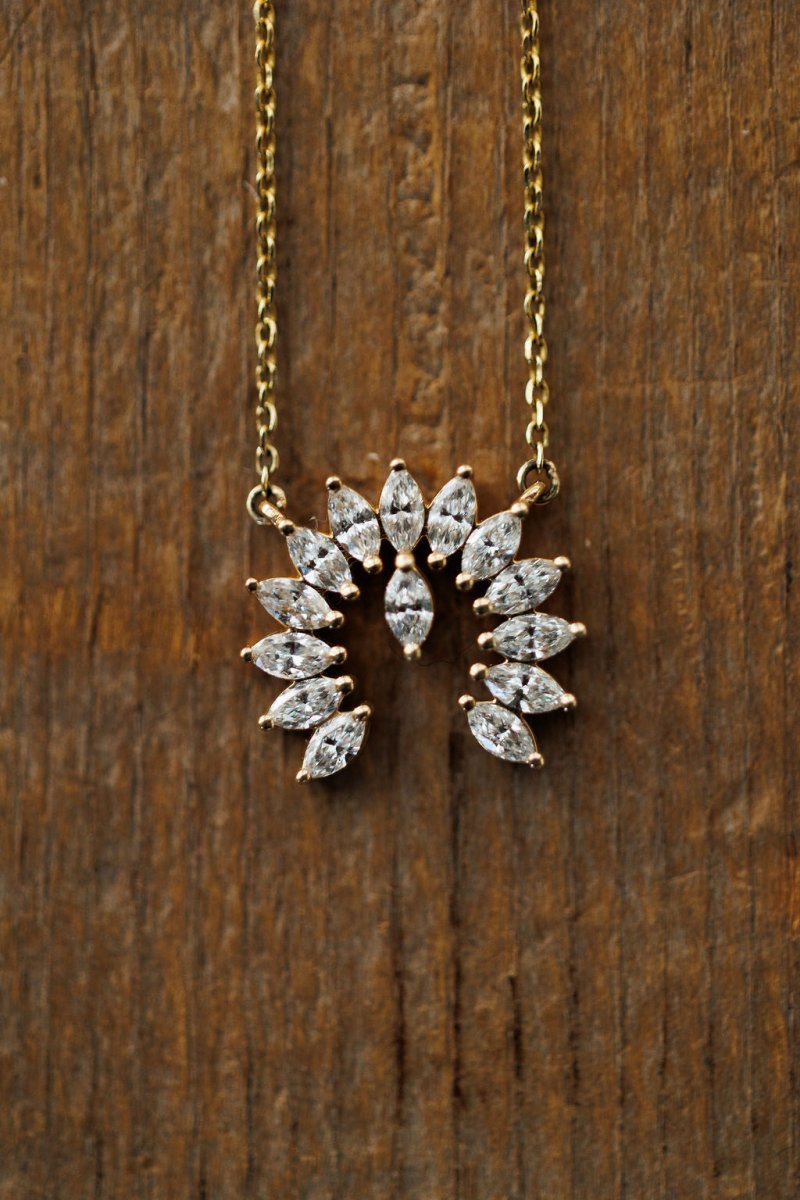 The Diamond Naja Necklace by Savannah Sevens western life{&}style features marquise-cut lab grown diamonds in a fan-pattern partial circle pendant, crafted in 14K gold and shown on a wooden background.