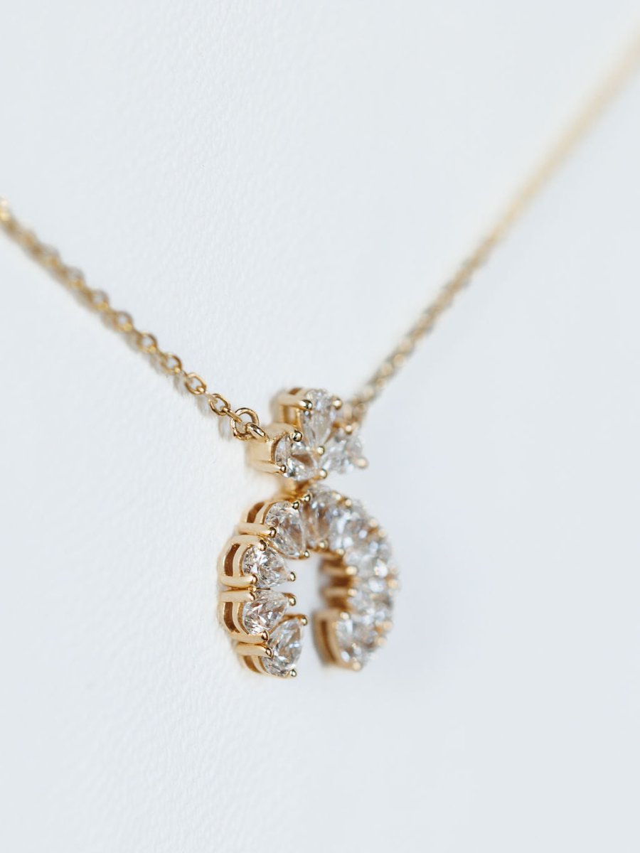 A close-up of the Savannah Sevens western life{&}style Diamond Squash Necklace in 14K gold, featuring a crescent pendant adorned with round and pear-shaped diamonds, displayed on a white background.