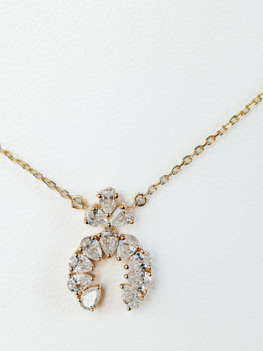 The Diamond Squash Necklace by Savannah Sevens western life{&}style is a 14K gold piece with a semi-circular pendant featuring multiple pear-shaped diamonds, shown against a white background.
