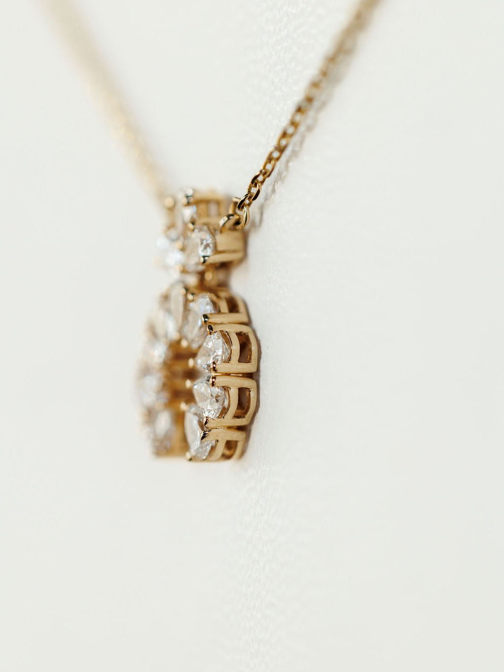 A close-up of the Diamond Squash Necklace by Savannah Sevens western life{&}style, featuring an intricate 14K gold pendant adorned with multiple sparkling lab grown diamonds against a soft, light background.