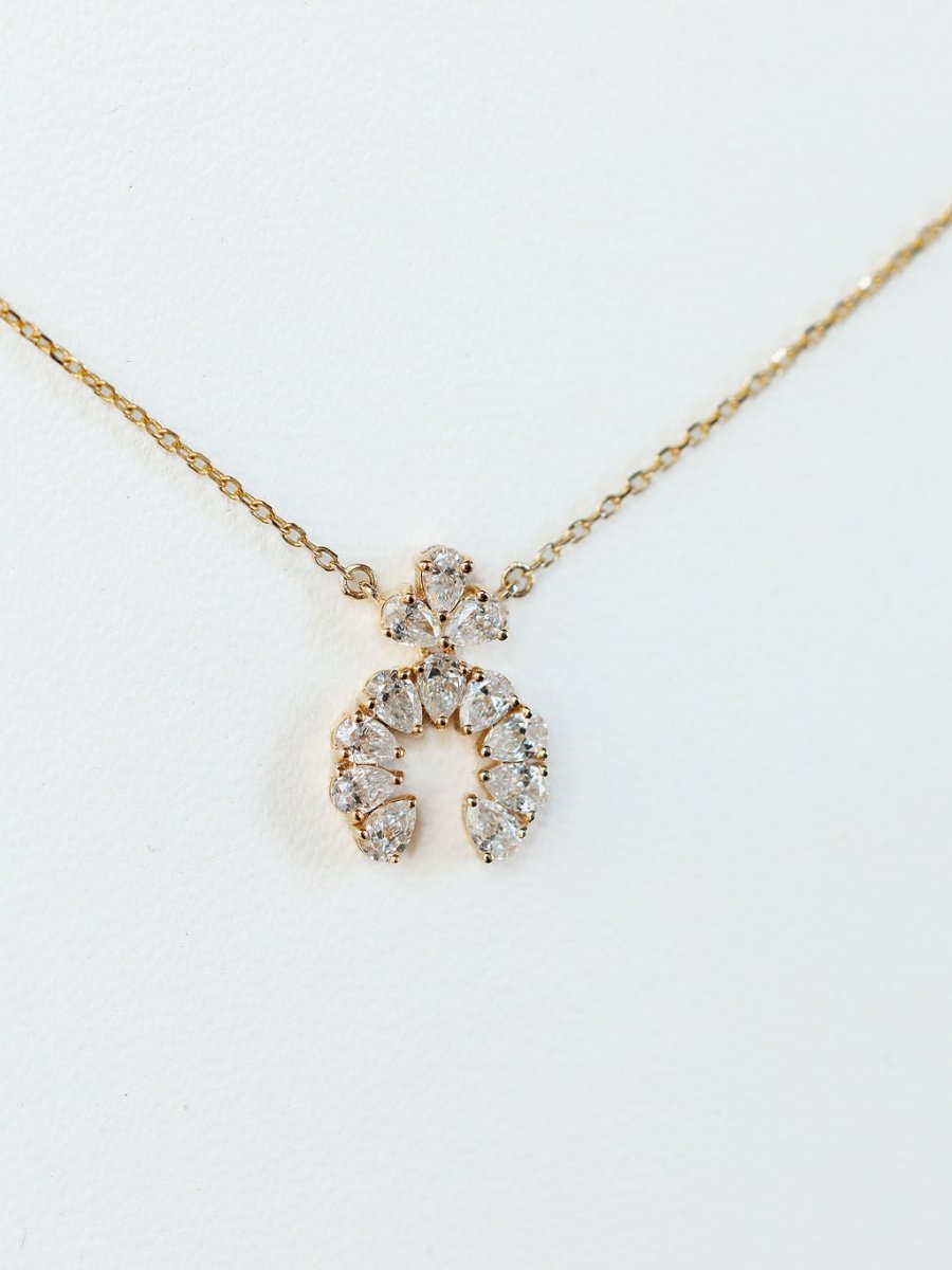 The Diamond Squash Necklace by Savannah Sevens western life{&}style features a 14K gold chain with a crescent-shaped pendant adorned with sparkling lab-grown and pear-shaped diamonds, showcased on a plain white background.