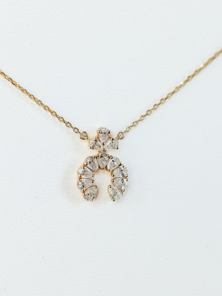The Diamond Squash Necklace by Savannah Sevens western life{&}style features a 14K gold chain with a crescent-shaped pendant adorned with sparkling lab-grown and pear-shaped diamonds, showcased on a plain white background.