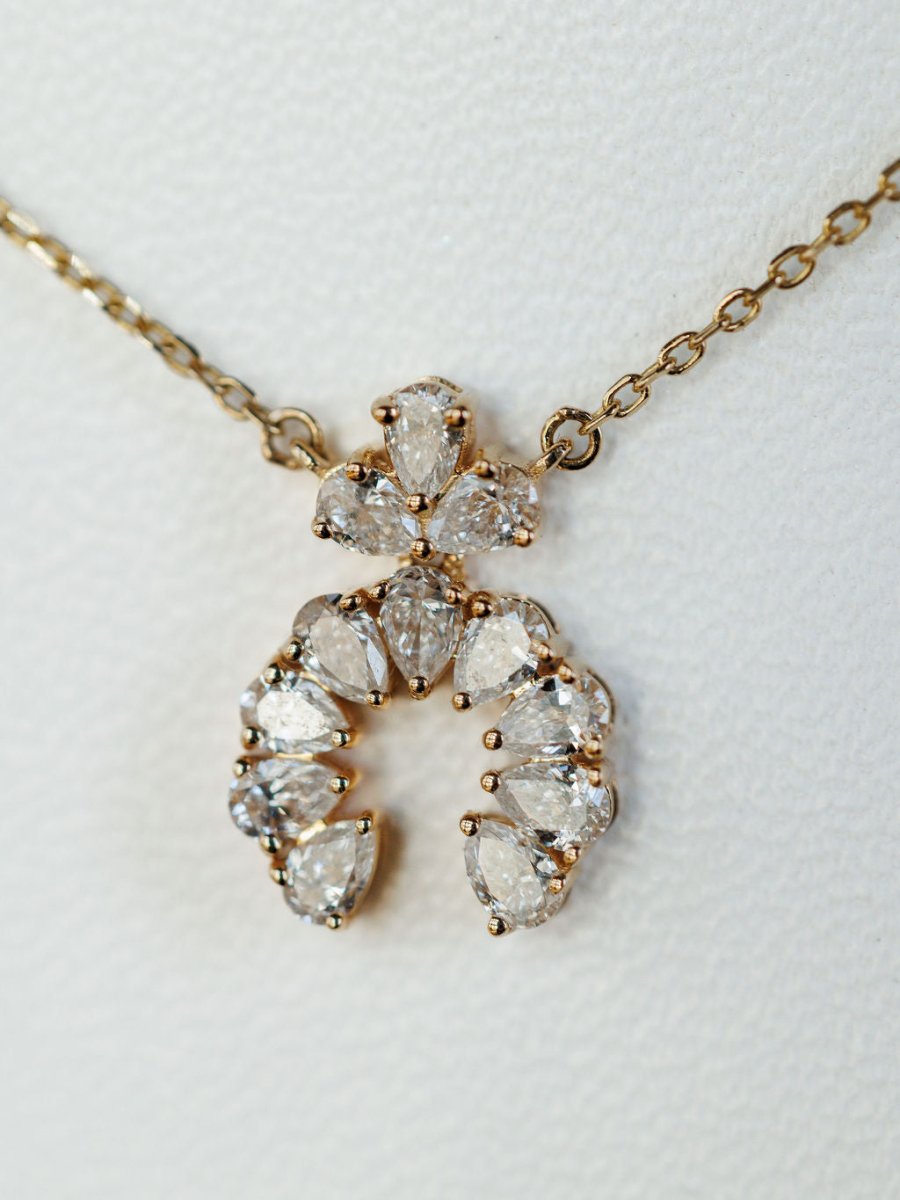 The Diamond Squash Necklace by Savannah Sevens western life{&}style features multiple pear-shaped diamonds in a decorative horseshoe design set in 14K gold, displayed on a textured white background.