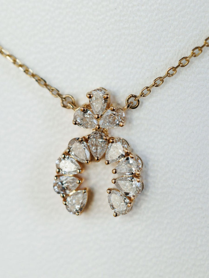 The Diamond Squash Necklace by Savannah Sevens western life{&}style features multiple pear-shaped diamonds in a decorative horseshoe design set in 14K gold, displayed on a textured white background.