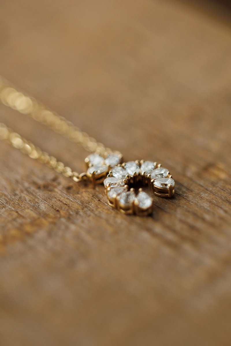 The Diamond Squash Necklace by Savannah Sevens western life{&}style features a 14K gold horseshoe-shaped pendant adorned with sparkling diamonds, elegantly displayed on a wooden surface.