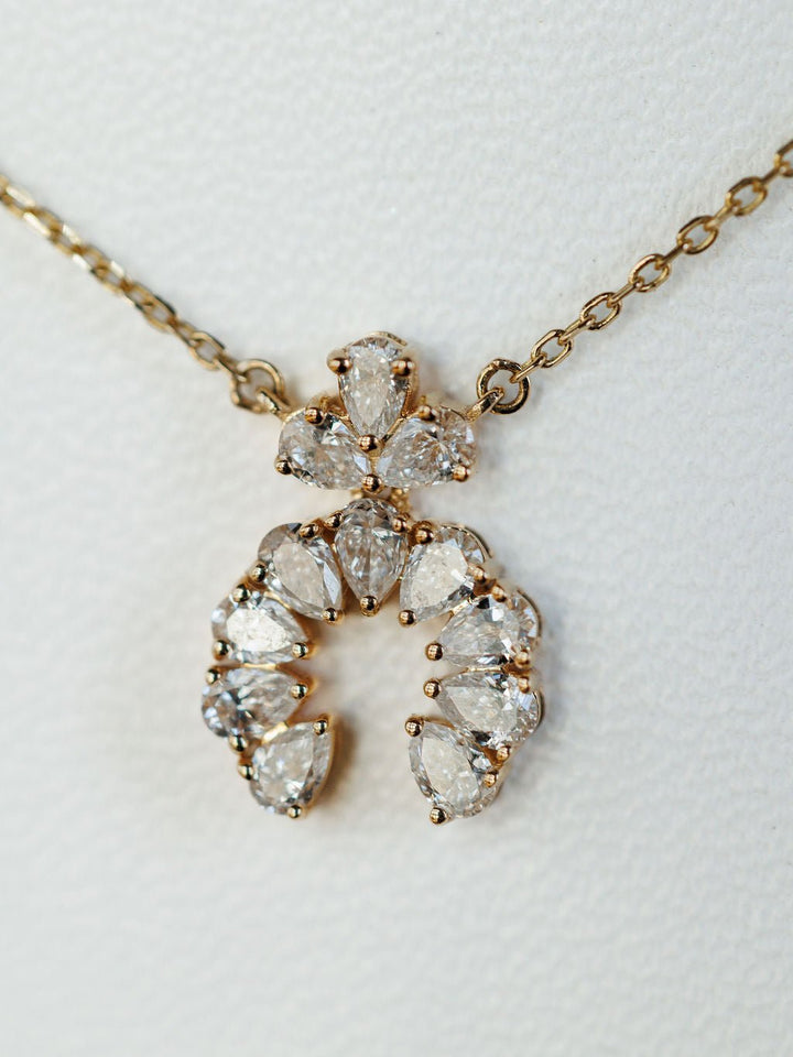 The Diamond Squash Necklace by Savannah Sevens western life{&}style features multiple pear-shaped diamonds in a decorative horseshoe design set in 14K gold, displayed on a textured white background.
