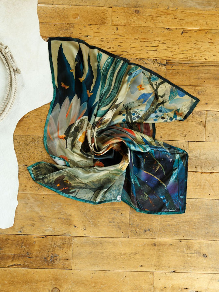 The Dolan Wild Rag by Savannah Sevens western life{&}style features vibrant, nature-inspired patterns with birds and butterflies, artfully laid on a wooden floor next to a white rug, infusing any space with Southwest charm.