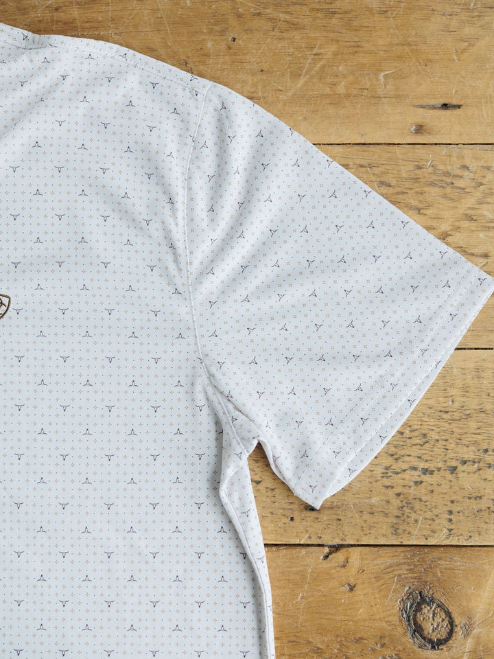 A close-up of the Dupree Ariat Men's Southwest Polo in light grey with a subtle geometric pattern by Savannah Sevens western life{&}style shows only the upper right, highlighting its moisture-wicking comfort on a wooden surface.