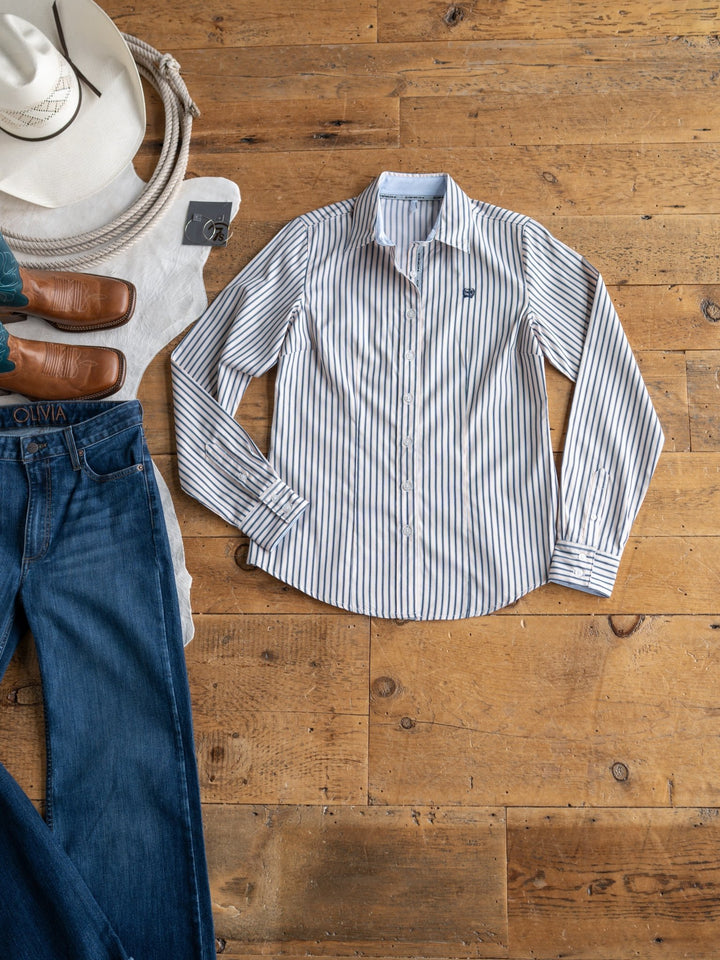 The Durant tencel top by Savannah Sevens western life&style is shown on a wooden floor with blue jeans, brown leather shoes, a cream hat, and a folded white sweater.