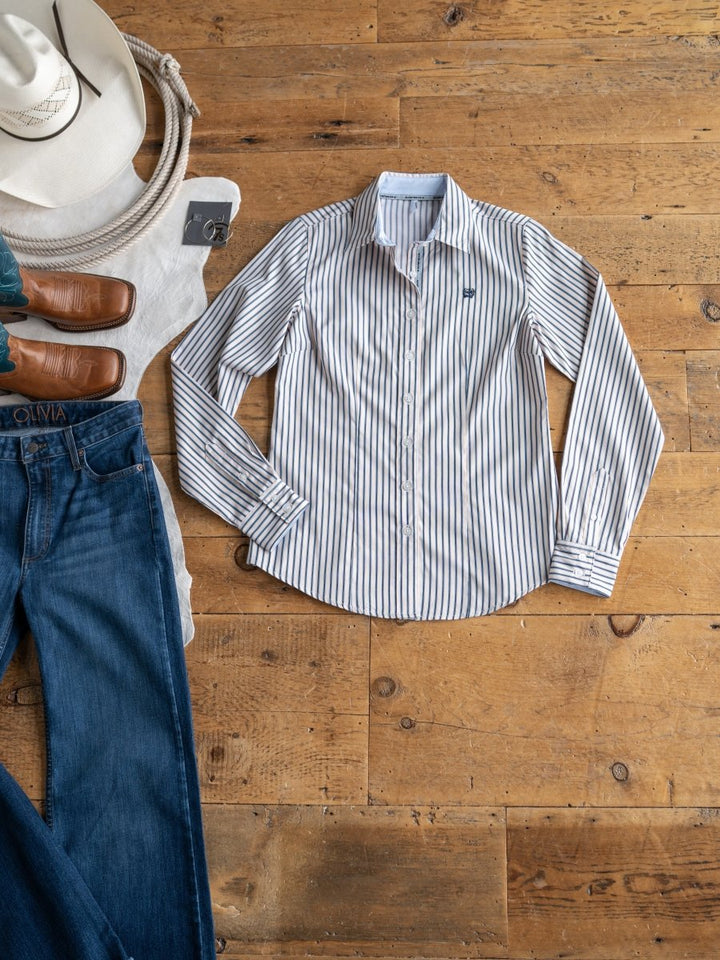 The Durant tencel top by Savannah Sevens western life&style is shown on a wooden floor with blue jeans, brown leather shoes, a cream hat, and a folded white sweater.
