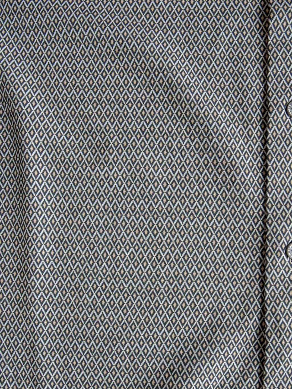Close-up of the Durham Wrangler Men's Southwest Button Up by Savannah Sevens western life{&}style, showcasing its small, repeating white and blue diamond pattern on a gray background. Visible folds and a portion of the button placket on the right emphasize this shirt’s subtle southwest-inspired style.