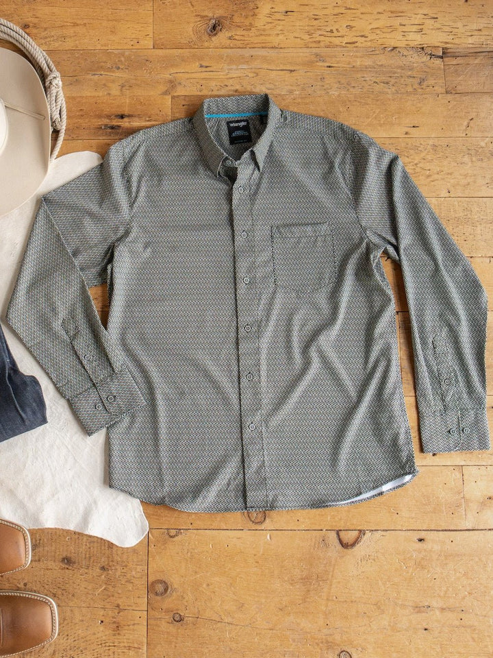 The Durham Wrangler Men's Southwest Button Up by Savannah Sevens western life{&}style, featuring a green southwest pattern and chest pocket, is displayed flat on a wooden floor beside a white hat and brown boots.