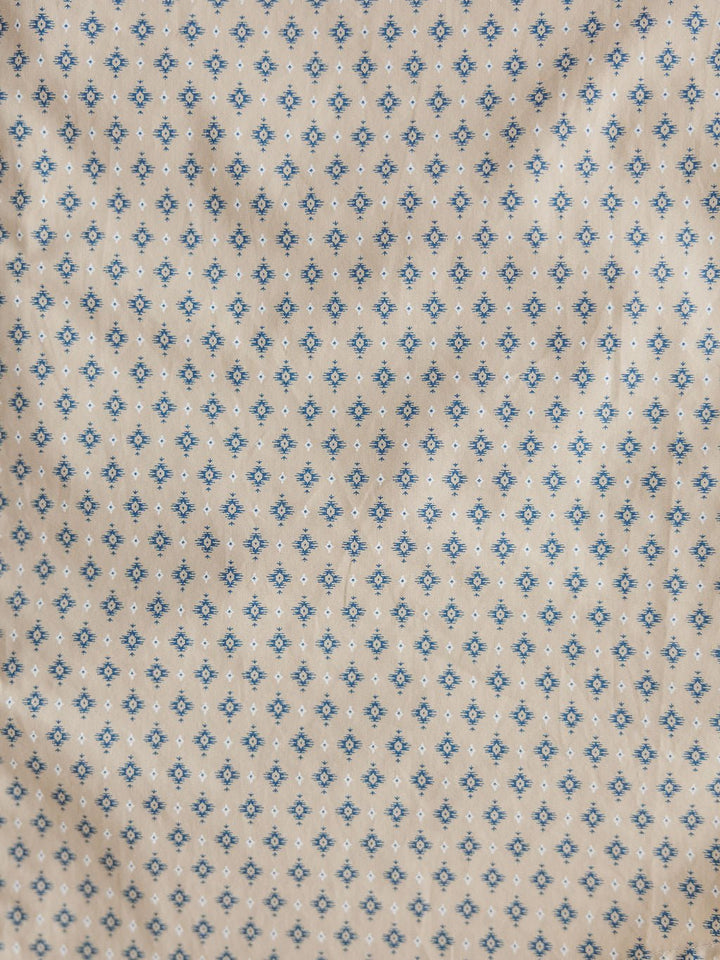 Close-up of beige fabric from the Easton Ariat Men's Southwest Button Up by Savannah Sevens western life{&}style, featuring a small blue and black geometric floral grid pattern with a slightly wrinkled, textured look.