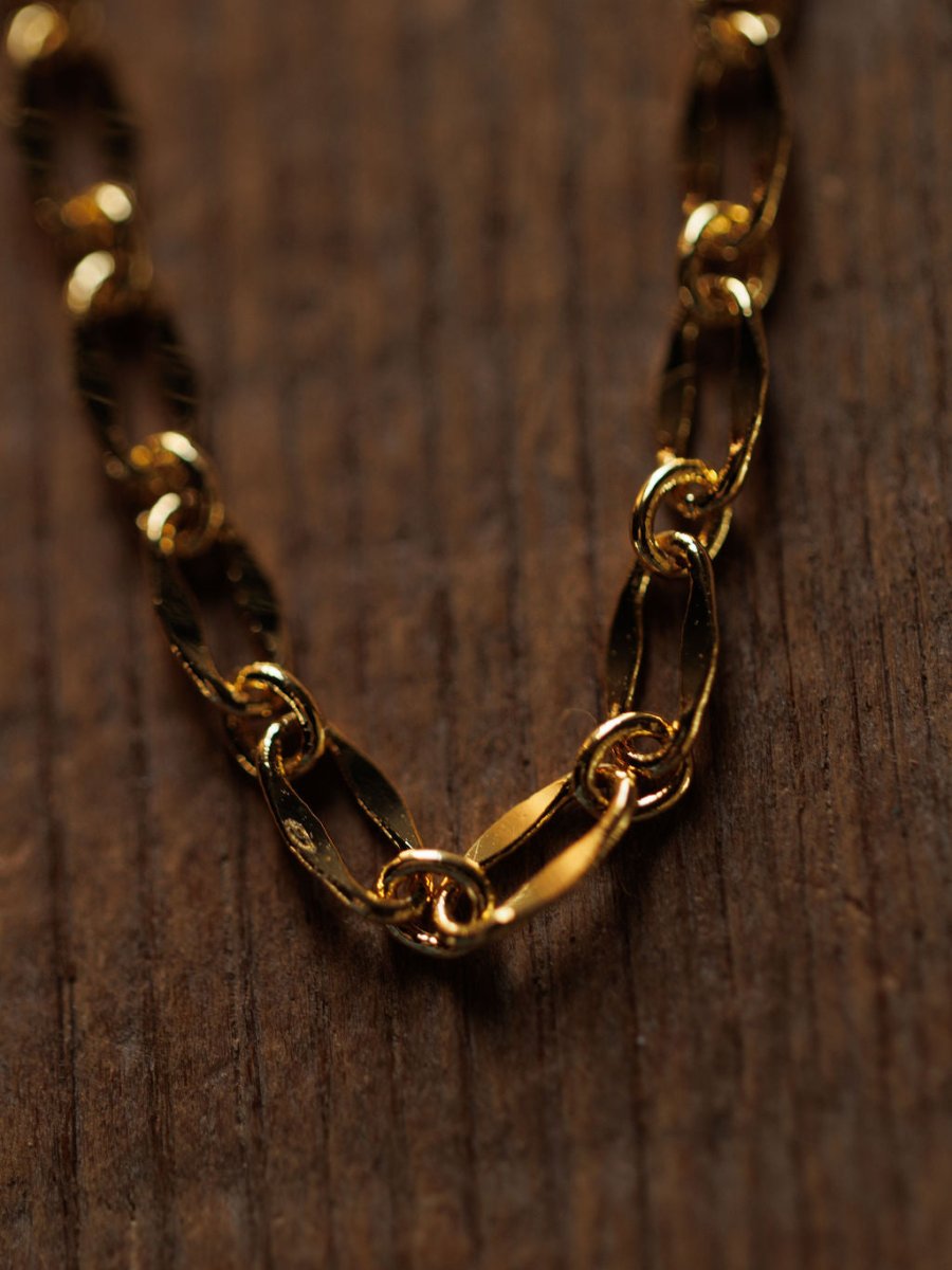 A close-up of the Eckley Necklace by Savannah Sevens western life{&}style—a gold choker with paperclip and oval links—resting on a textured wooden surface.