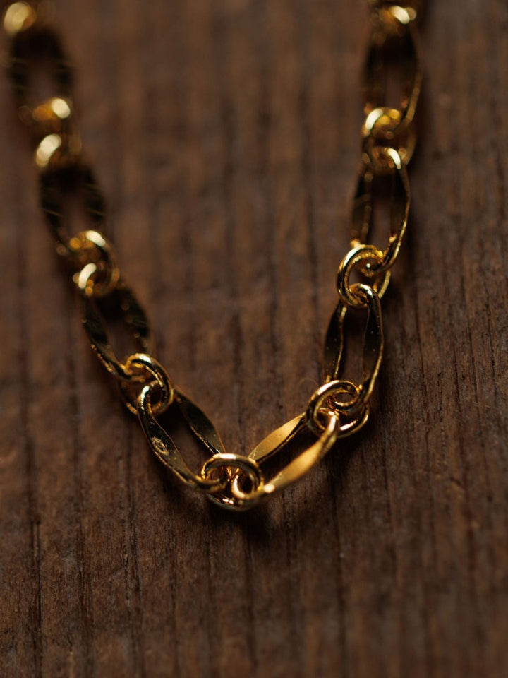 A close-up of the Eckley Necklace by Savannah Sevens western life{&}style—a gold choker with paperclip and oval links—resting on a textured wooden surface.