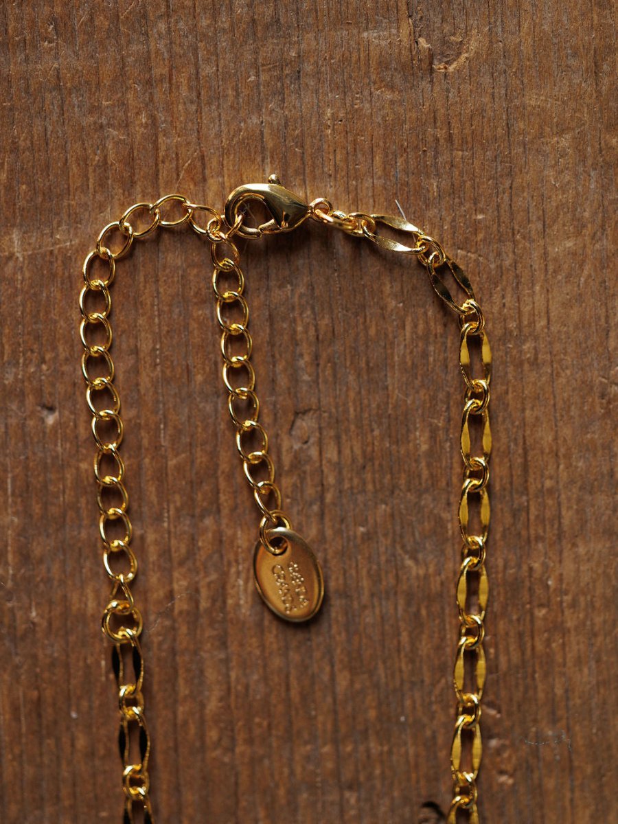 A close-up of the Eckley Necklace by Savannah Sevens western life{&}style, featuring an 18K gold filled paperclip design, lobster clasp, extender chain, and small oval tag on a textured wooden surface.