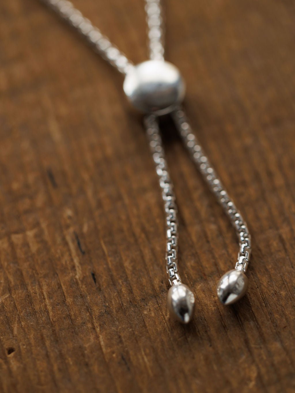 A close-up of the Elida Bracelet by Savannah Sevens western life{&}style, crafted in sterling silver with a round slider bead and two pointed ends, displayed on a textured wooden surface.