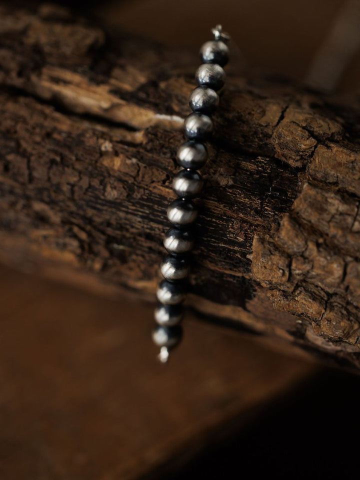 The Elida Bracelet by Savannah Sevens western life{&}style, crafted in sterling silver with beaded accents, is displayed atop rugged dark wood with a softly blurred warm brown backdrop.