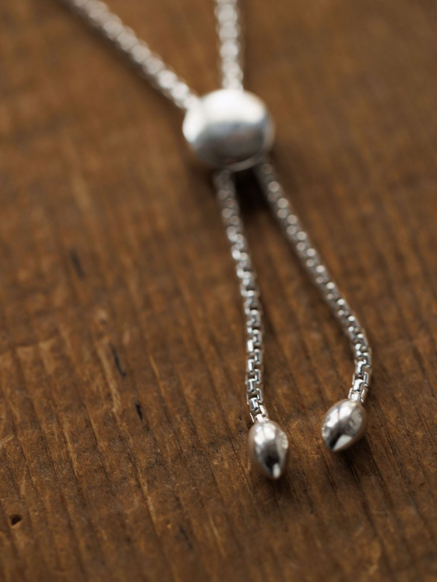 A close-up of the Elida Bracelet by Savannah Sevens western life{&}style, crafted in sterling silver with a round slider bead and two pointed ends, displayed on a textured wooden surface.