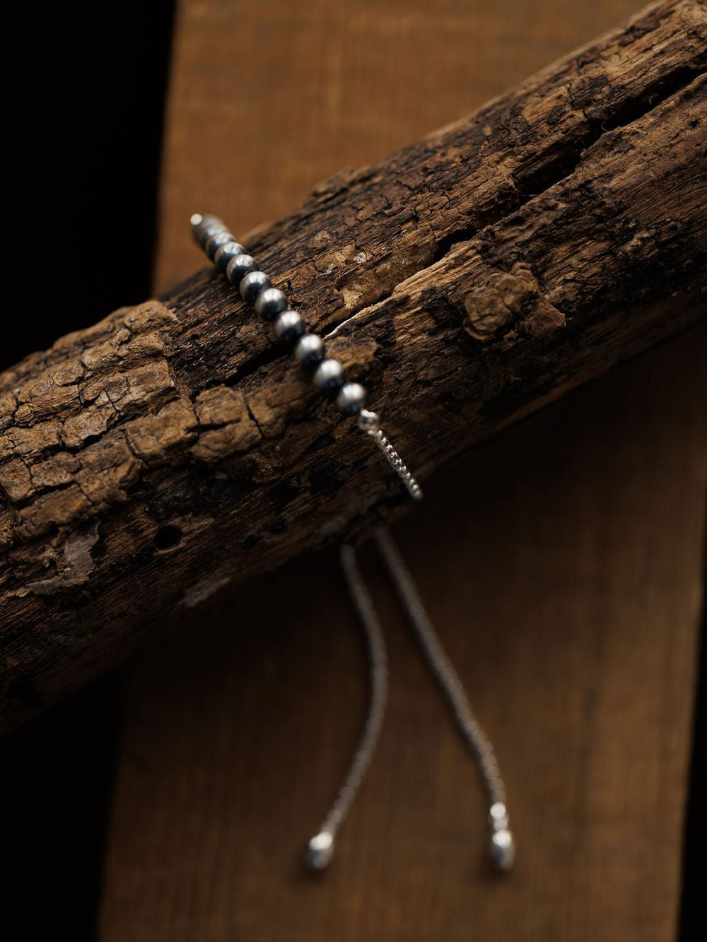 The Elida Bracelet by Savannah Sevens western life{&}style, featuring Navajo pearls and an adjustable chain, is displayed on rugged wood for a rustic yet elegant contrast.