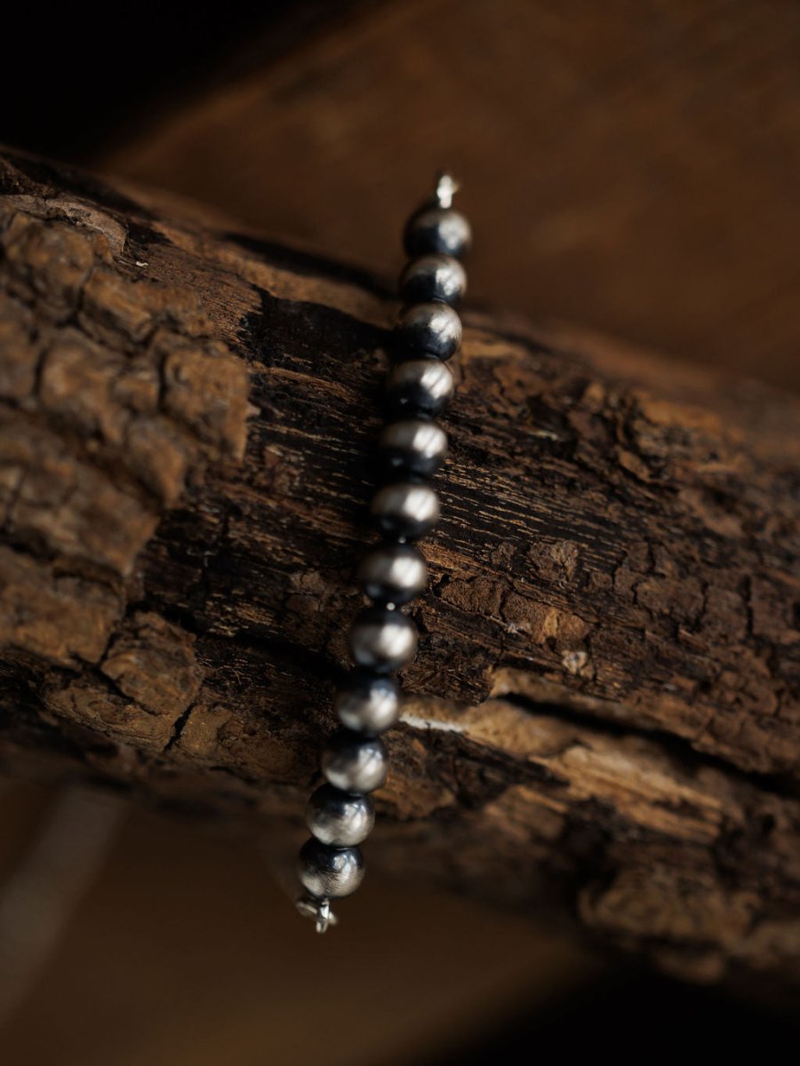 A close-up of the Elida Bracelet by Savannah Sevens western life{&}style, featuring round metallic dark grey beads, draped over textured rough wood. The softly blurred background highlights the sterling silver and wood grain.