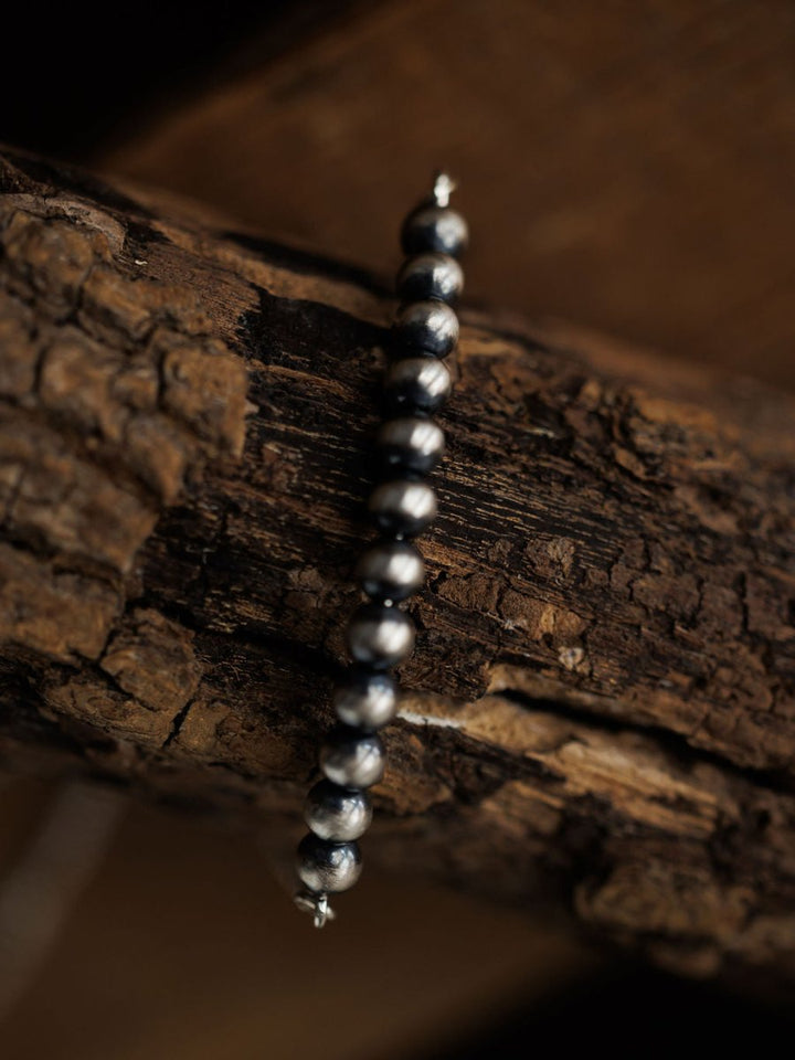 A close-up of the Elida Bracelet by Savannah Sevens western life{&}style, featuring round metallic dark grey beads, draped over textured rough wood. The softly blurred background highlights the sterling silver and wood grain.