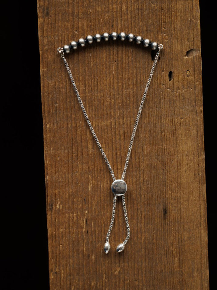 The Elida Bracelet by Savannah Sevens western life{&}style is a sterling silver beaded adjustable bracelet with a sliding clasp, shown vertically on rustic wood. This elegant piece adds timeless style to any look.