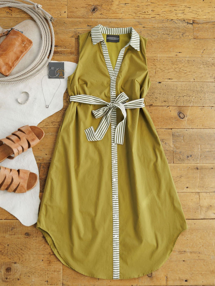 The Elida Chartreuse Striped Dress by Savannah Sevens western life{&}style, a sleeveless midi with white and green trim, collar, and adjustable waist tie, is displayed beside tan sandals, a rope bag, sunglasses, brown pouch, and necklace on a wooden floor.