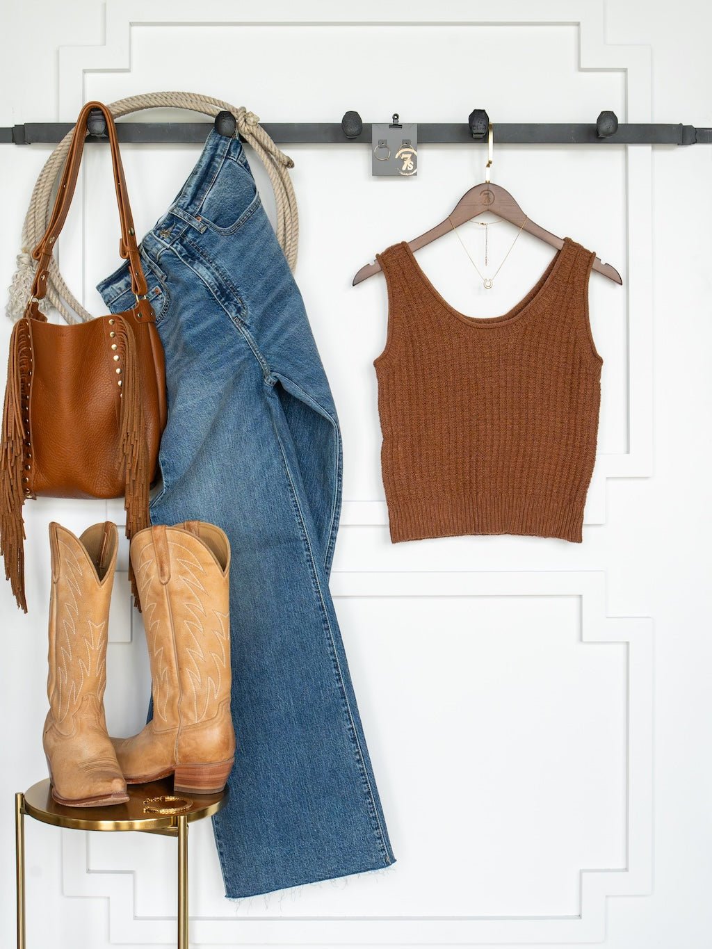 Ellaville Sienna Knit Sleeveless Top by Savannah Sevens western life{&}style on a hanger, paired with blue jeans, tan cowboy boots, and a brown fringe purse, are displayed on a white wall with a black rail. This combination creates a coordinated, casual Western-inspired outfit.