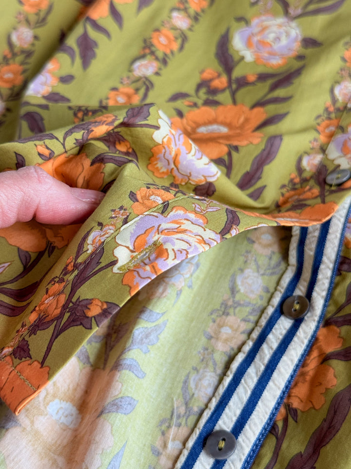 A hand lifts the Ellington Chartreuse Floral Top by Savannah Sevens western life{&}style, revealing a blue-striped puff sleeve blouse with blue buttons underneath.