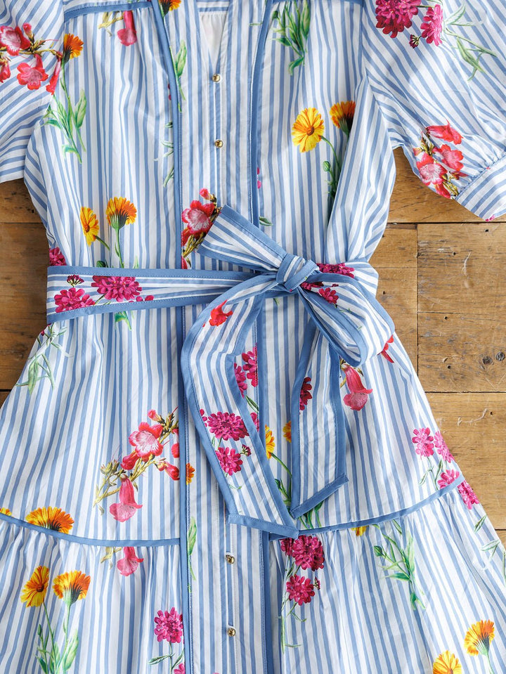 The Ellinwood Floral Striped Cotton Dress by Savannah Sevens western life{&}style, featuring blue and white stripes, colorful floral prints, short sleeves, and a matching belt, is displayed flat on a wooden surface.