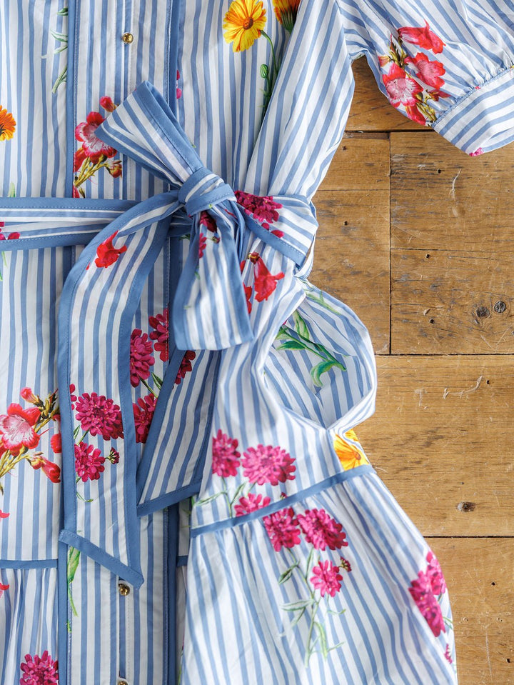 The Ellinwood Floral Striped Cotton Dress by Savannah Sevens western life{&}style features blue-and-white stripes, vibrant red, pink, and yellow floral prints, a tied waist sash, and short sleeves—perfect for adding charm to your summer wardrobe.