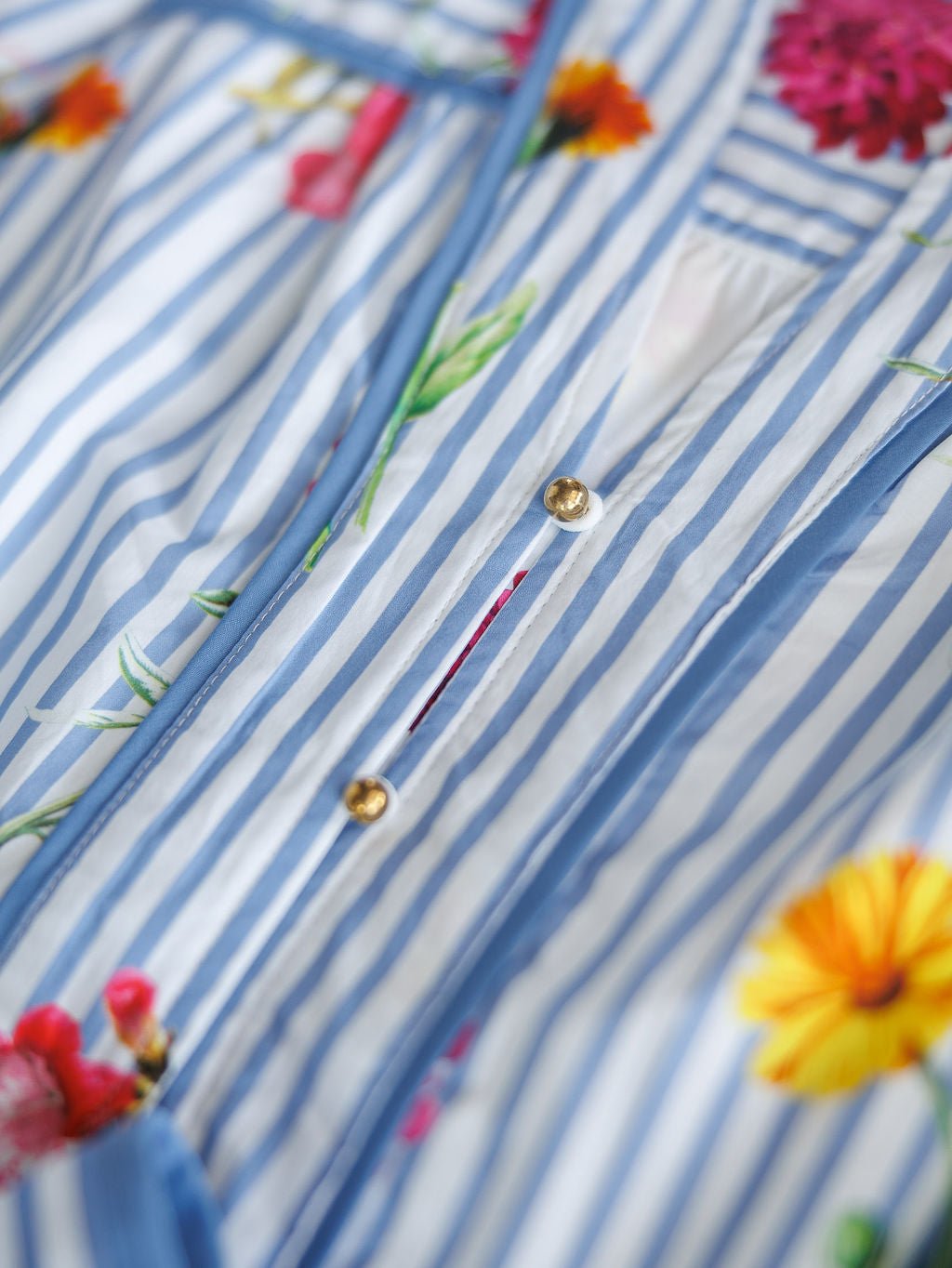 Close-up of the Ellinwood Floral Striped Cotton Dress by Savannah Sevens western life{&}style, featuring blue and white stripes, colorful floral patterns, and gold buttons.