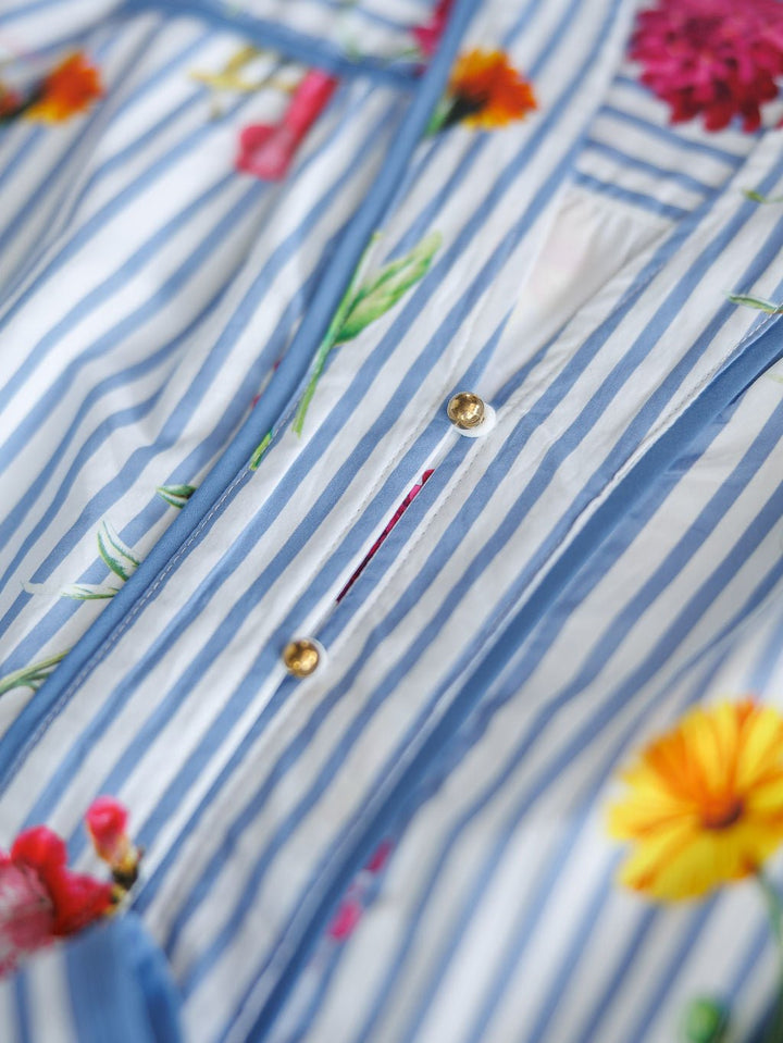 Close-up of the Ellinwood Floral Striped Cotton Dress by Savannah Sevens western life{&}style, featuring blue and white stripes, colorful floral patterns, and gold buttons.