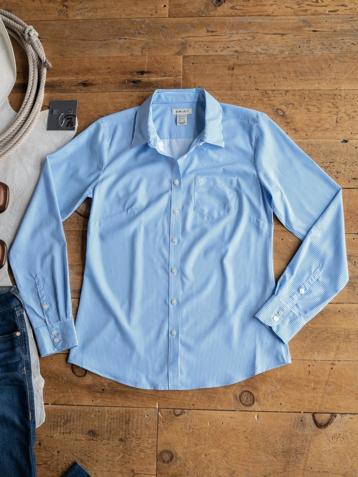The Ellisville by Savannah Sevens western life{&}style: a light blue pinstripe, long-sleeve button-up shirt with subtle white stripes, displayed with jeans, sunglasses, and a white bag—stylish sun protection for any occasion.